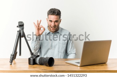 Young handsome photography teacher winks an eye and holds an okay gesture with hand.