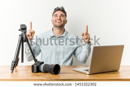 Young handsome photography teacher indicates with both fore fingers up showing a blank space.