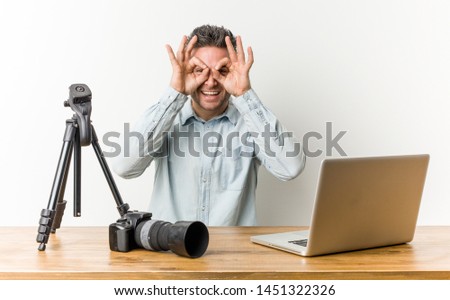 Young handsome photography teacher showing okay sign over eyes