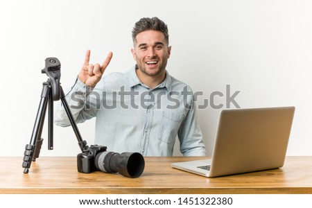 Young handsome photography teacher showing a horns gesture as a revolution concept.