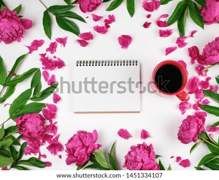 empty open notebook in a cage and a red cup of coffee on a white background, along the perimeter of blooming red peonies, top view