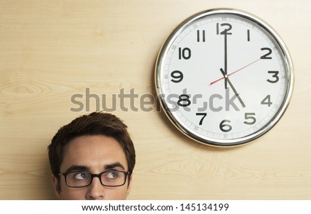 Young businessman wearing spectacles looking at clock on wooden wall in office Royalty-Free Stock Photo #145134199
