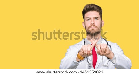 Young handsome doctor man wearing medical coat Rejection expression crossing fingers doing negative sign