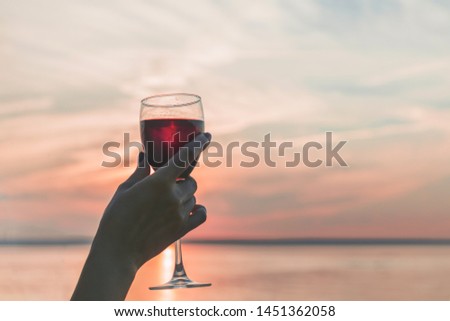 
Glass of red wine in the female hand at sunset sky