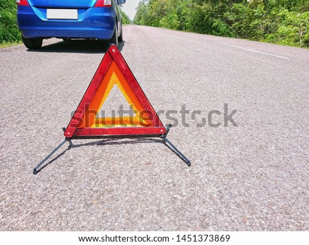Emergency red warning triangle on the road sign with a blue broken car