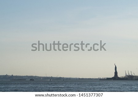 Seascape landscape view of the Statue of Liberty silhouette in the horizon, with cranes next to it, sea in first plan and wide blue sky in background, Staten Island, Manhattan, New York, America, USA.