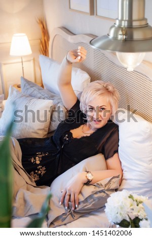 The beautiful young woman with blonde hair lies in the bed at home.