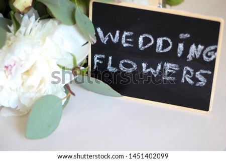 Wedding flowers calligraphy template text for your design illustration concept. Handwritten lettering title words on  black isolated background. White peonies on a light background stock photo. Shop