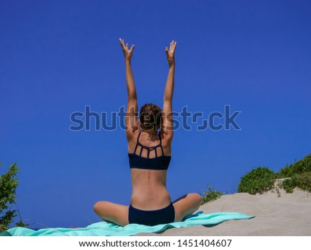 Slim and athletic girl in a black bikini practicing yoga pose before a wonderful blue sky on a sandy beach. Suitable for Fitness, Wellness, Yoga, Sports, Health, Cosmetics, Body care.
