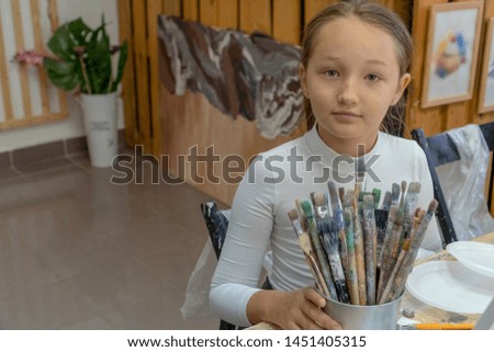 A set of different color brushes in the hands of the girl. Interior of the art school for drawing children. Creativity and people concept