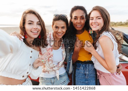 Picture of amazing smiling optimistic young cheery women friends posing near car outdoors at the beach.