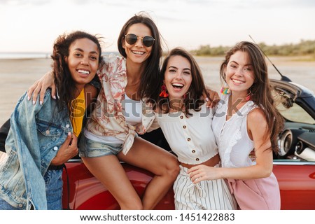 Picture of amazing young happy smiling cheery women friends posing near car outdoors at the beach.