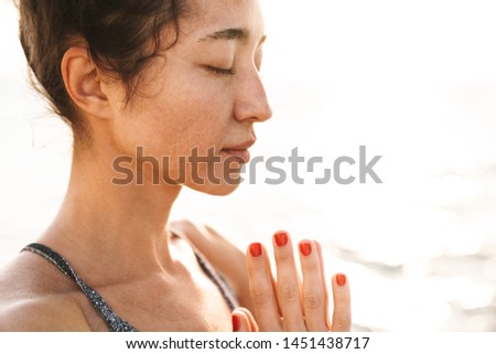 Photo of caucasian fitness woman in tracksuit meditating and keeping palms together while practicing yoga in morning outdoors