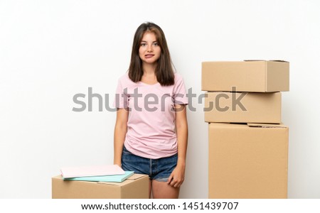 Young girl moving in new home among boxes having doubts and with confuse face expression