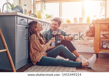 Love is in the air. Beautiful young couple drinking wine while sitting on the kitchen floor at home Royalty-Free Stock Photo #1451449214