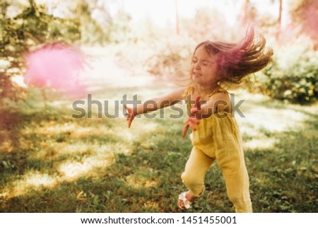 Horizontal outdoors image of beautiful little girl with long blonde hair, playing in the park with magical pink dust for fairy tale concept. Happy child dancing on her birthday party in the garden.