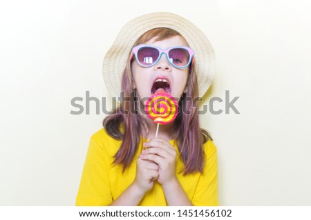 The child is holding a lollipop. Childish joy is sweetness. Little girl in a yellow T-shirt and glasses.
