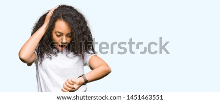 Young beautiful girl with curly hair wearing casual white t-shirt Looking at the watch time worried, afraid of getting late