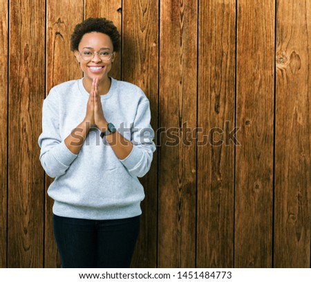 Young beautiful african american woman wearing glasses over isolated background praying with hands together asking for forgiveness smiling confident.