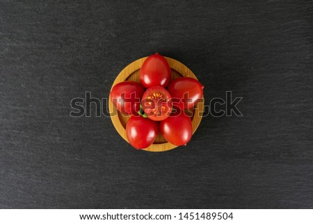 Group of five whole one half of fresh red tomato cherry on a bamboo plate flatlay on grey stone