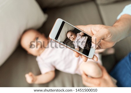 family, technology and fatherhood concept - close up of middle aged father with smartphone taking picture of his little baby daughter lying on sofa at home