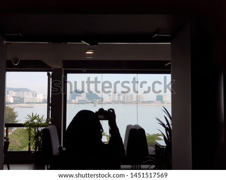 Silhouette of a woman taking photos of a cityscape by the bay