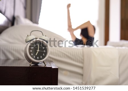 Closeup alarm clock and blurred woman stretching arm in bed after wake up in the morning Royalty-Free Stock Photo #1451539277