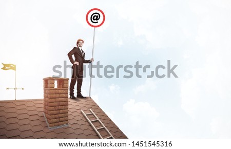 Young businessman on house roof with roadsign in hand. Mixed media