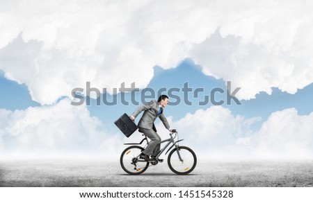 Man wearing business suit riding bicycle outdoor. Cyclist with suitcase on background of blue sky. Time management and business activity. Businessman hurrying to work. Business competition and career