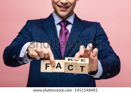 cropped view of businessman holding wooden cubes with fake fact lettering on pink background