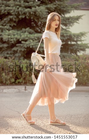 
The beautiful blonde girl in a fashionable pink tulle skirt and white top is walking in the rays of the setting sun and waves the valans in a skirt, laughs a lot and enjoys life. Romantic concept.  