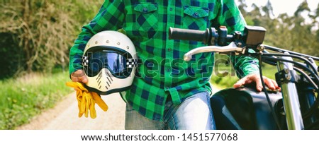 Unrecognizable young man posing with motorcycle, helmet and gloves in the middle of the road