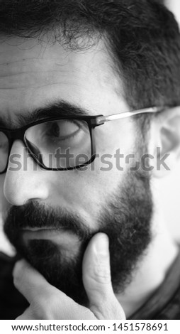 Black and white extreme close up portrait of a  man with serious facial expression touching his chin. Male showing no emotion looking  forward on a white background. Vertical photo