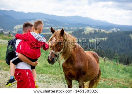 man with kid pet the horse mountains on background. travel concept