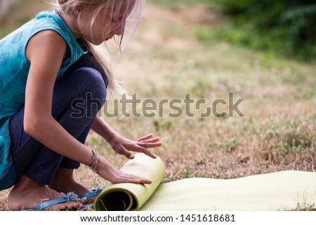 Blond caucasian girl rolling yoga mat. Close-up of attractive young girl folding green yoga mat. Healthy, exercise concept. Kids yoga concept. girl is practicing yoga. Healthy lifestyle.