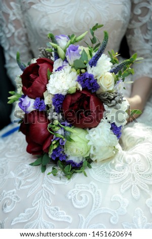 Bouquet of red and white peonies and roses in the hands of the bride in a white dress with lace