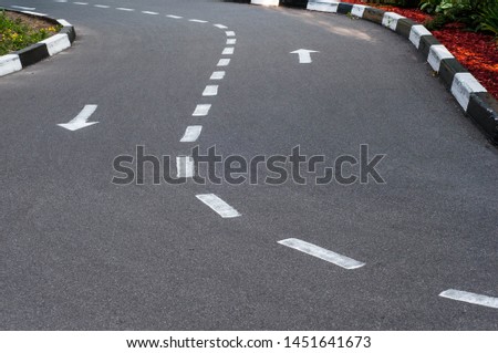 Asphalt road with a two-way marking and a curb.  White arrows indicate the direction of travel.