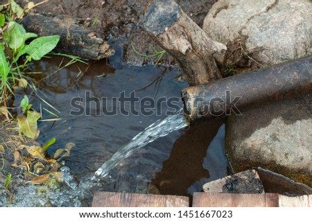 Source of water on the bank of the river - clear water pours from a pipe against the background of earth and grass