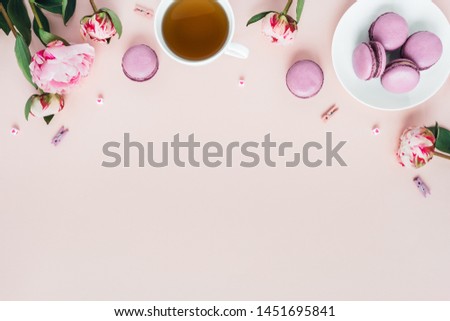 Pink background with macaroons and a Cup of tea surrounded by peonies. Top view with space for your text.
