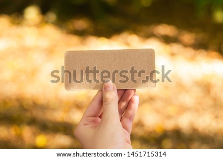 Hand holding empty card in autumn park in sunny rays.  Background. Copy space.
