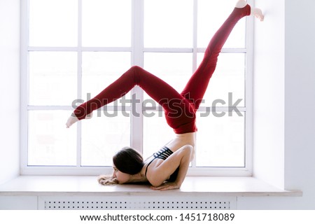 Yoga girl in red tights near the window on a white background