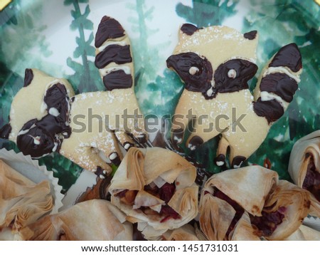 Sweet Christmas Biscuits. Raccoons as Sweet Cakes on The Plate with Landscape Picture in Home Kitchen.