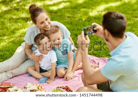 family, leisure and people concept - father taking picture of happy mother with two little sons by smartphone on picnic at summer park