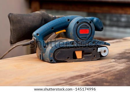 A belt sander tool on a wooden surface with saw dust
