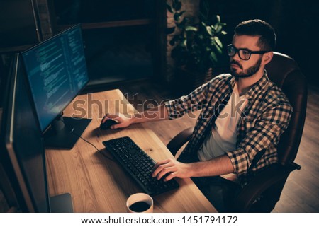 Close up photo not smiling handsome he him his guy coder typing php css keyboard development outsource IT processing language two monitors table office agency wear specs formalwear plaid shirt