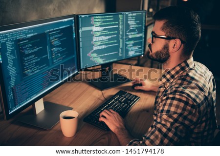 Close up side profile photo handsome he him his guy brainstorming briefing coder typing php css keyboard development outsource IT two monitors table office agency wear specs formalwear plaid shirt