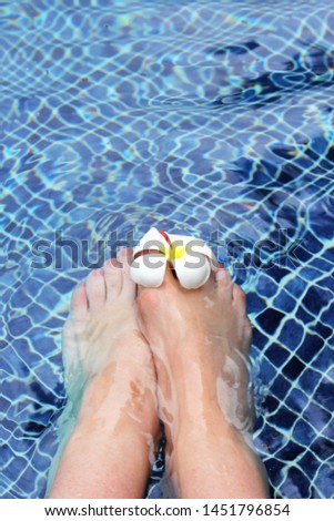 Beautiful female foot feet in swimming pool travel background with white Spa frangipani flowers - stock Image poolside photo