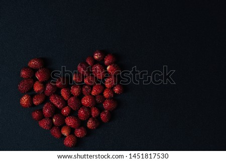 Ripe berries of wild strawberries in the form of hearts on a black background.Top view.