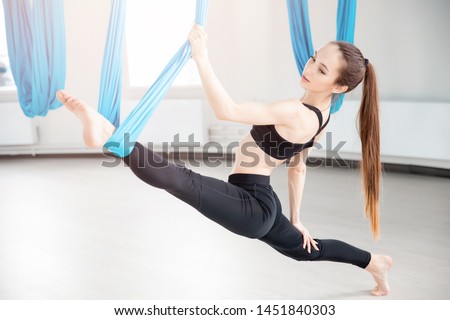 Young woman performing antigravity aerial yoga exercise in white studio.