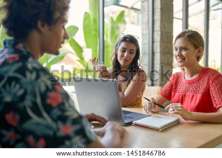 Candid lifestyle shot of three diverse millennial friends working together on laptop computer in bright modern cafe